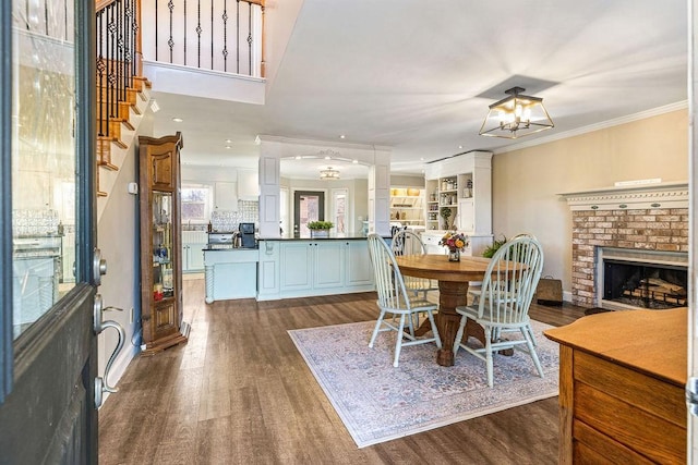 dining room featuring a brick fireplace, crown molding, decorative columns, and dark hardwood / wood-style floors