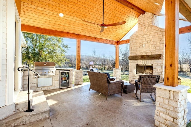 view of patio featuring a grill, beverage cooler, an outdoor stone fireplace, exterior kitchen, and ceiling fan