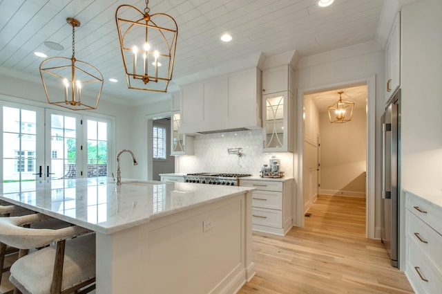 kitchen featuring pendant lighting, sink, white cabinets, a chandelier, and a kitchen island with sink