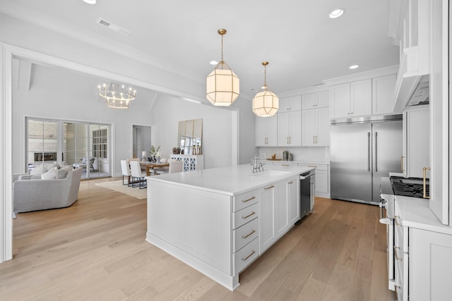 kitchen with white cabinetry, pendant lighting, stainless steel appliances, and an island with sink