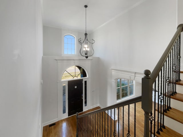 foyer with a towering ceiling, ornamental molding, hardwood / wood-style floors, and a notable chandelier