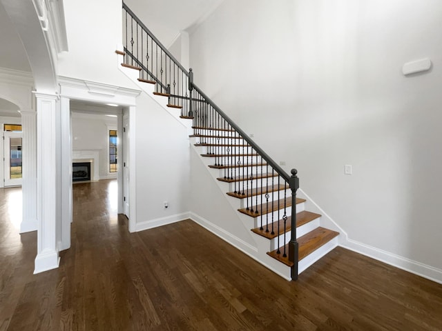 stairway featuring hardwood / wood-style flooring, ornamental molding, a towering ceiling, and ornate columns