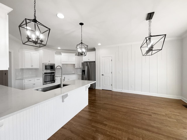 kitchen with a breakfast bar, appliances with stainless steel finishes, white cabinetry, hanging light fixtures, and ornamental molding