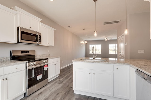 kitchen with appliances with stainless steel finishes, pendant lighting, white cabinetry, sink, and light stone countertops