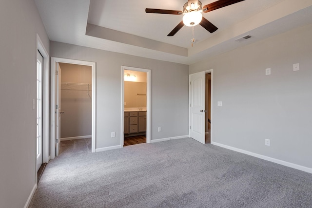 unfurnished bedroom featuring ensuite bathroom, dark colored carpet, a spacious closet, a raised ceiling, and a closet