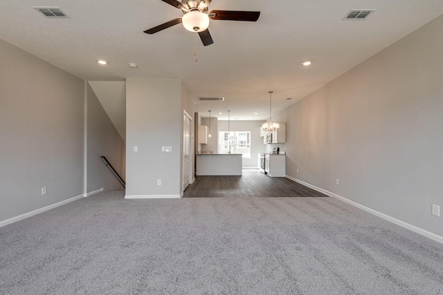 unfurnished living room with dark carpet and ceiling fan with notable chandelier