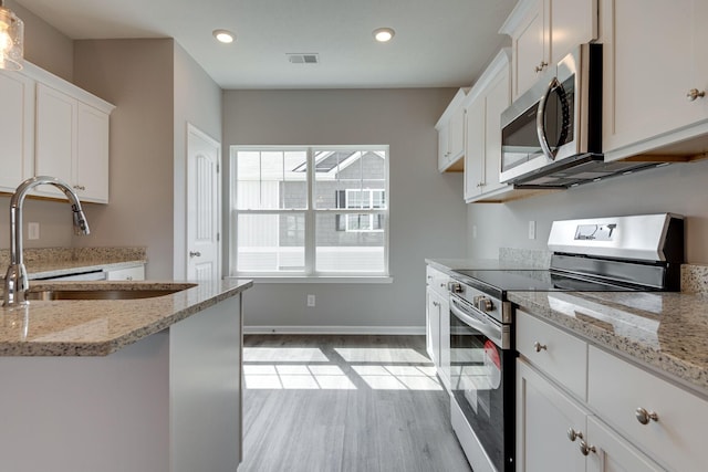 kitchen featuring appliances with stainless steel finishes, white cabinetry, sink, light hardwood / wood-style floors, and light stone countertops