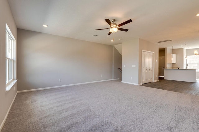 unfurnished living room featuring ceiling fan and dark colored carpet