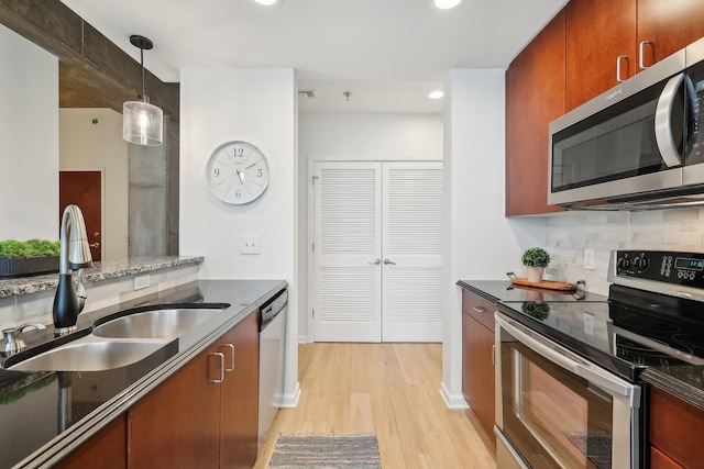 kitchen with sink, tasteful backsplash, decorative light fixtures, stainless steel appliances, and light hardwood / wood-style floors