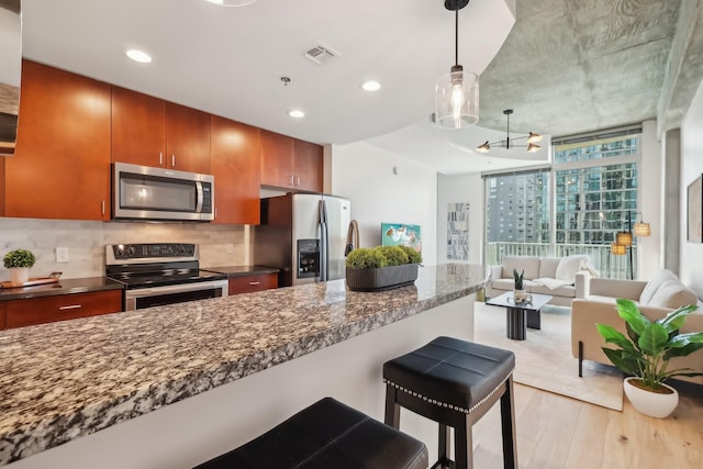 kitchen with light hardwood / wood-style flooring, a breakfast bar area, hanging light fixtures, stainless steel appliances, and decorative backsplash