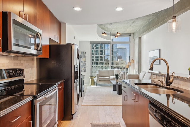 kitchen featuring floor to ceiling windows, sink, decorative light fixtures, stainless steel appliances, and light hardwood / wood-style floors