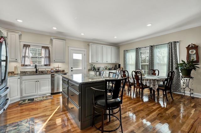 kitchen with a kitchen island, sink, white cabinets, stainless steel dishwasher, and light stone counters