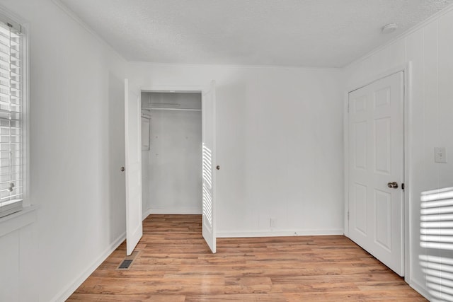 unfurnished bedroom featuring a closet, ornamental molding, a textured ceiling, and light wood-type flooring