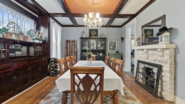 dining area featuring beamed ceiling, coffered ceiling, light hardwood / wood-style floors, and a stone fireplace