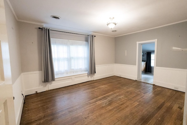 empty room featuring crown molding, a wainscoted wall, wood-type flooring, and visible vents