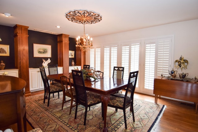 dining space with ornate columns, wood-type flooring, and a chandelier