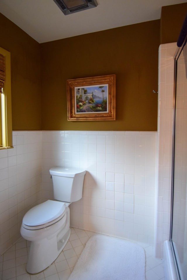 bathroom with a shower with door, tile walls, tile patterned floors, and toilet