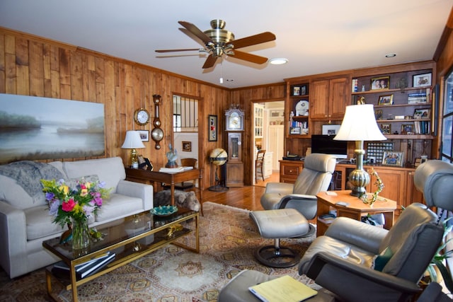 living room featuring ceiling fan, ornamental molding, wooden walls, and wood-type flooring