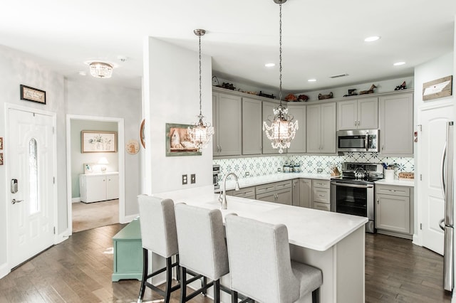 kitchen with a kitchen bar, tasteful backsplash, hanging light fixtures, appliances with stainless steel finishes, and kitchen peninsula