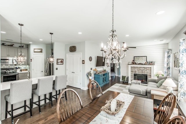 dining room with wooden walls, dark wood-type flooring, an inviting chandelier, and a fireplace