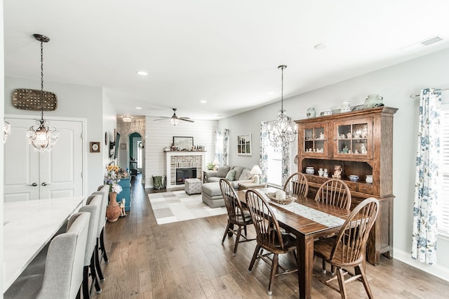 dining area with ceiling fan with notable chandelier, a fireplace, and wood-type flooring