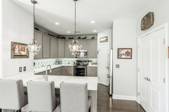 kitchen with gray cabinets, a kitchen breakfast bar, hanging light fixtures, kitchen peninsula, and stainless steel appliances