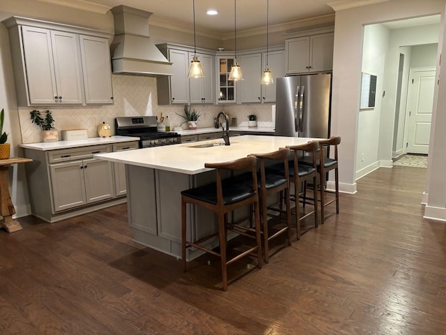 kitchen featuring premium range hood, appliances with stainless steel finishes, decorative light fixtures, sink, and a center island with sink