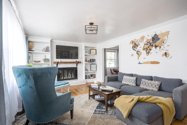 living room with built in shelves, ornamental molding, hardwood / wood-style floors, and a brick fireplace