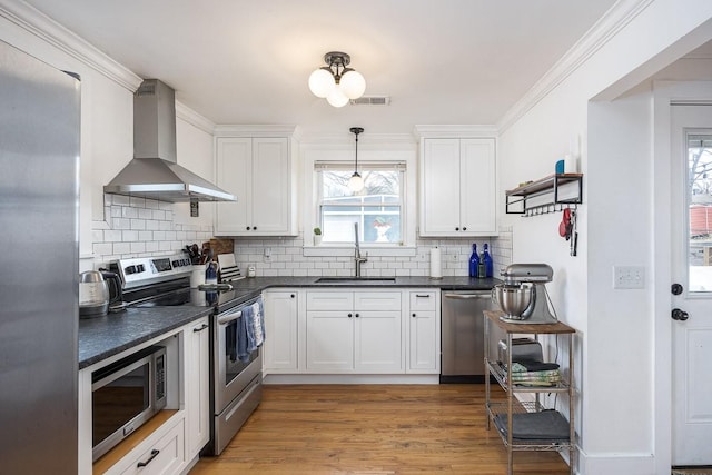 kitchen with stainless steel appliances, sink, wall chimney range hood, and white cabinets