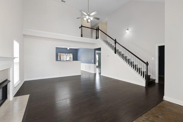 unfurnished living room featuring a fireplace, dark hardwood / wood-style floors, ceiling fan, and a high ceiling