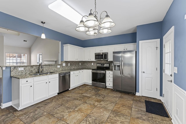 kitchen featuring sink, dark stone countertops, appliances with stainless steel finishes, pendant lighting, and white cabinets