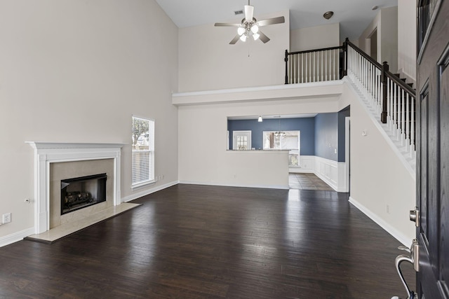 unfurnished living room featuring a high ceiling, a premium fireplace, dark hardwood / wood-style floors, and ceiling fan