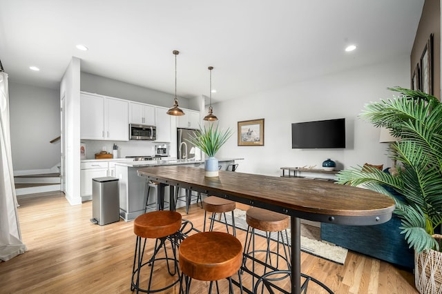 kitchen featuring white cabinetry, hanging light fixtures, a kitchen island with sink, stainless steel appliances, and light hardwood / wood-style floors