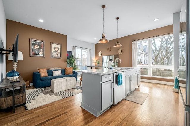 kitchen with sink, decorative light fixtures, light wood-type flooring, dishwasher, and an island with sink