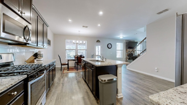 kitchen with appliances with stainless steel finishes, decorative light fixtures, an island with sink, sink, and light stone countertops