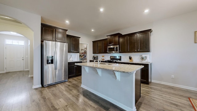 kitchen with stainless steel appliances, a center island with sink, a kitchen bar, and light hardwood / wood-style flooring