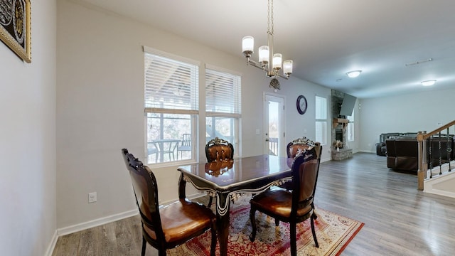 dining room with wood-type flooring, a stone fireplace, and a notable chandelier