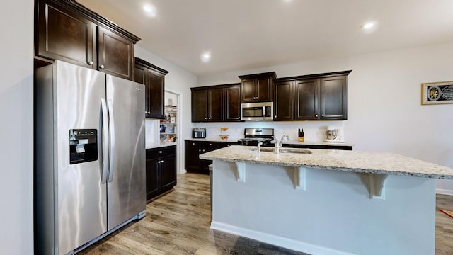 kitchen featuring appliances with stainless steel finishes, an island with sink, sink, backsplash, and dark brown cabinets