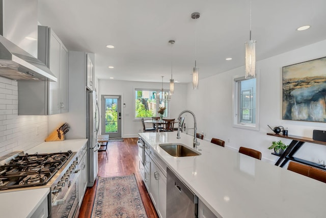 kitchen featuring sink, backsplash, hanging light fixtures, stainless steel appliances, and wall chimney exhaust hood