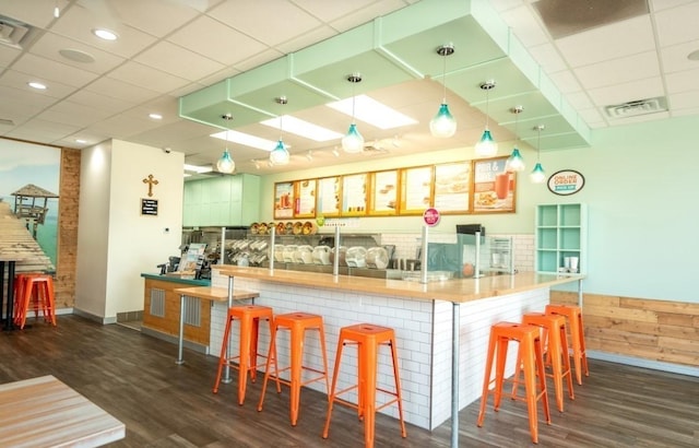 kitchen with hanging light fixtures, a breakfast bar, dark wood-type flooring, and a drop ceiling