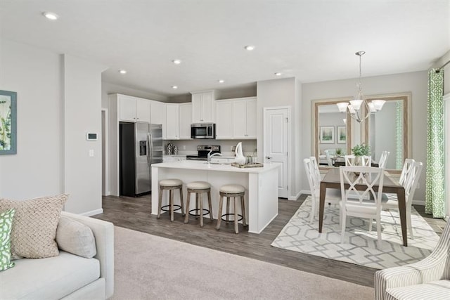 kitchen with appliances with stainless steel finishes, a breakfast bar, decorative light fixtures, an island with sink, and a notable chandelier