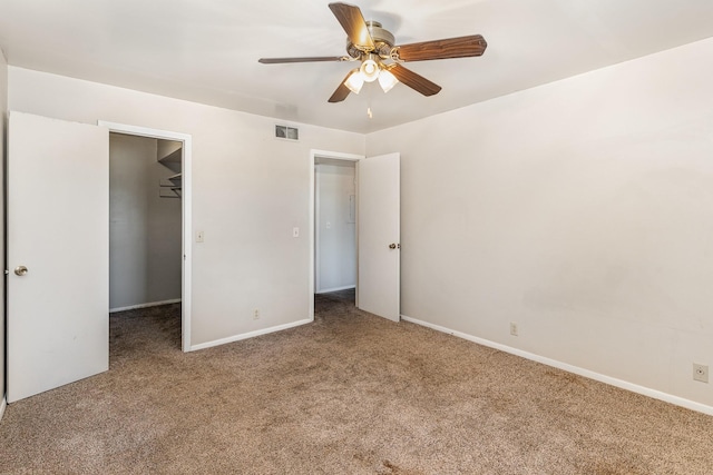 unfurnished bedroom featuring a spacious closet, a closet, ceiling fan, and carpet flooring