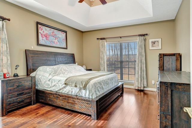 bedroom with wood-type flooring, ceiling fan, and a tray ceiling