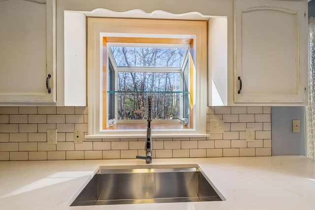 kitchen with white cabinetry, sink, backsplash, and light stone countertops