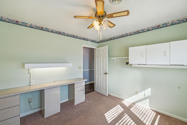 unfurnished office with ceiling fan, built in desk, light colored carpet, and a textured ceiling