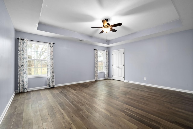 empty room with a raised ceiling, a healthy amount of sunlight, and dark wood-type flooring