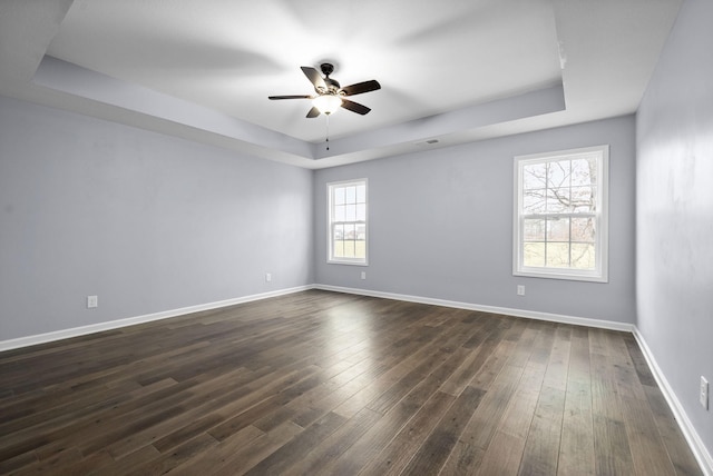 empty room with a raised ceiling, dark hardwood / wood-style floors, and ceiling fan