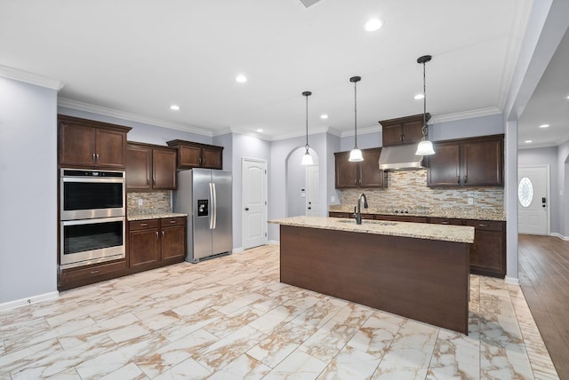 kitchen with sink, decorative light fixtures, dark brown cabinets, appliances with stainless steel finishes, and wall chimney range hood