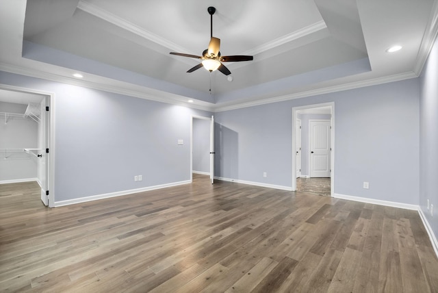 unfurnished bedroom featuring hardwood / wood-style flooring, a tray ceiling, a spacious closet, and crown molding