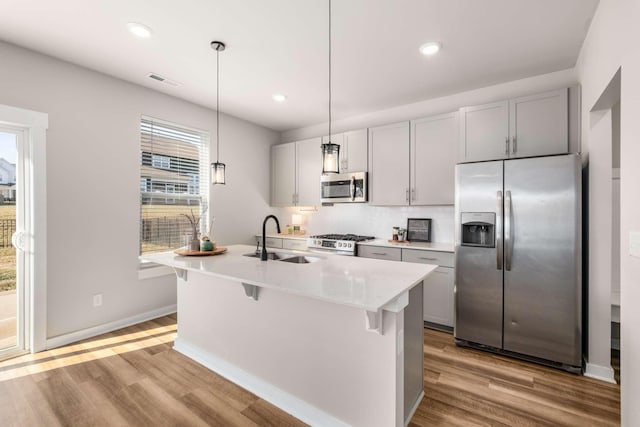 kitchen featuring appliances with stainless steel finishes, decorative light fixtures, sink, a kitchen island with sink, and light wood-type flooring